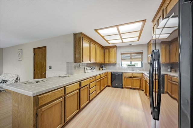 kitchen with black appliances, tile counters, tasteful backsplash, kitchen peninsula, and light hardwood / wood-style flooring