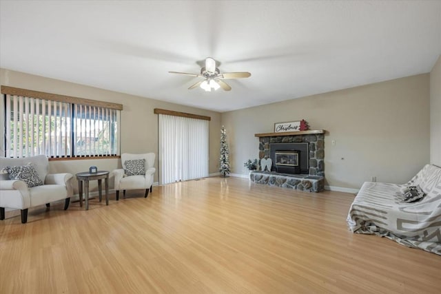 sitting room featuring ceiling fan, a stone fireplace, and light wood-type flooring