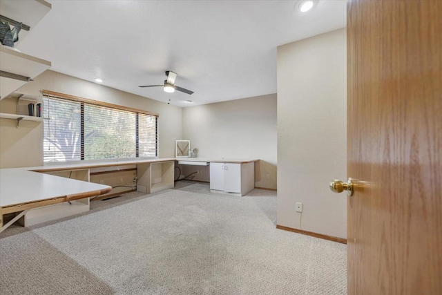 unfurnished office featuring light carpet, ceiling fan, and built in desk