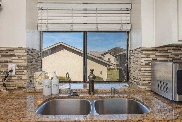 room details featuring tasteful backsplash, sink, white cabinets, and dark stone counters