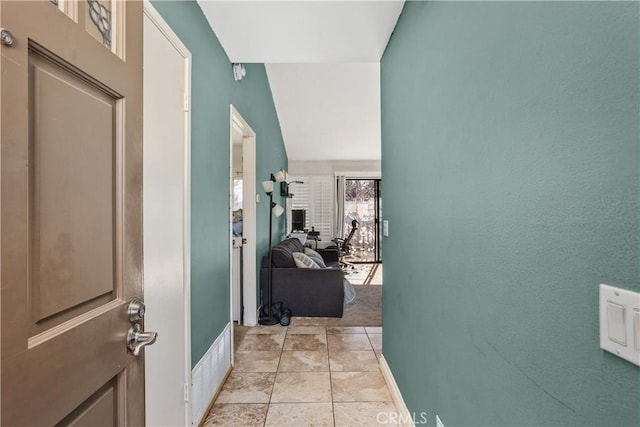 hallway with light tile patterned floors and vaulted ceiling