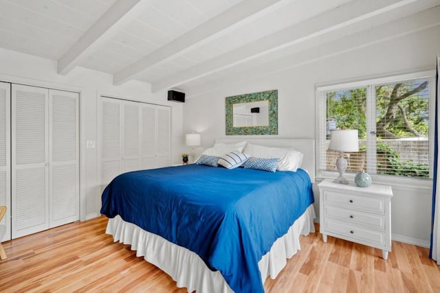 bedroom with beam ceiling, light hardwood / wood-style floors, and two closets