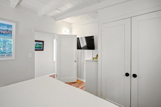 bedroom featuring beamed ceiling, light hardwood / wood-style flooring, and a closet