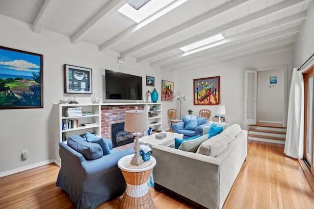 living room with beam ceiling, a skylight, light wood-type flooring, and a brick fireplace