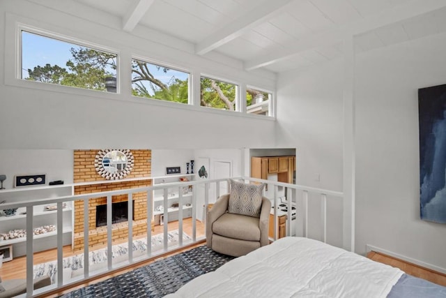 bedroom with wood-type flooring, lofted ceiling with beams, a brick fireplace, and multiple windows