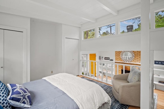 bedroom with a fireplace, wood-type flooring, multiple windows, and beamed ceiling