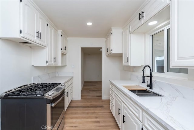 kitchen with gas range, light hardwood / wood-style flooring, white cabinets, and sink