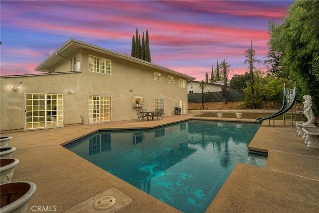 pool at dusk with a patio and a water slide