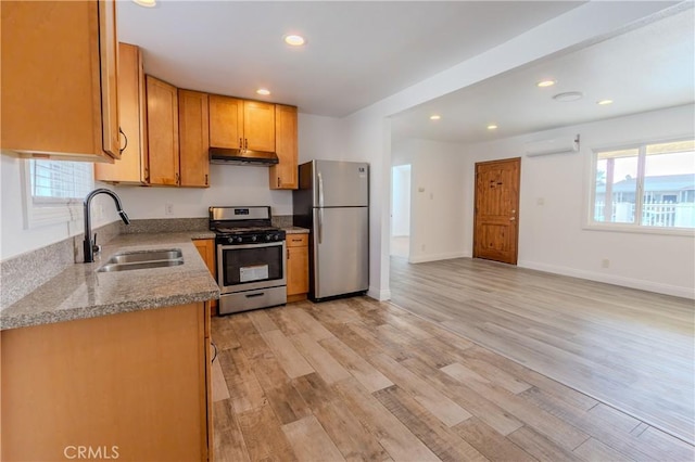 kitchen with light stone countertops, sink, stainless steel appliances, a wall mounted air conditioner, and light wood-type flooring