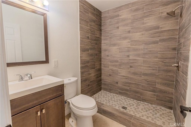 bathroom featuring a tile shower, tile patterned floors, vanity, and toilet