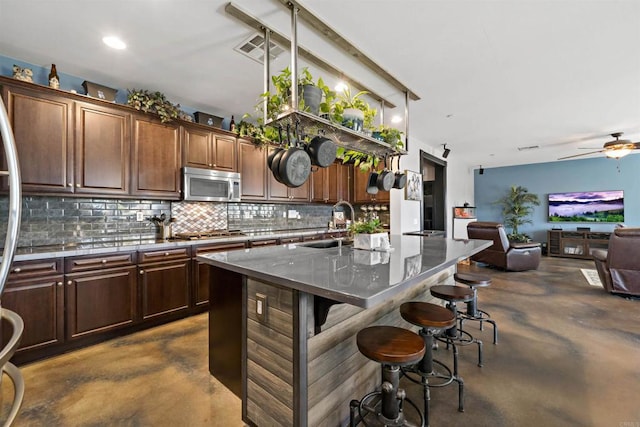 kitchen with an island with sink, stainless steel appliances, tasteful backsplash, ceiling fan, and a kitchen bar