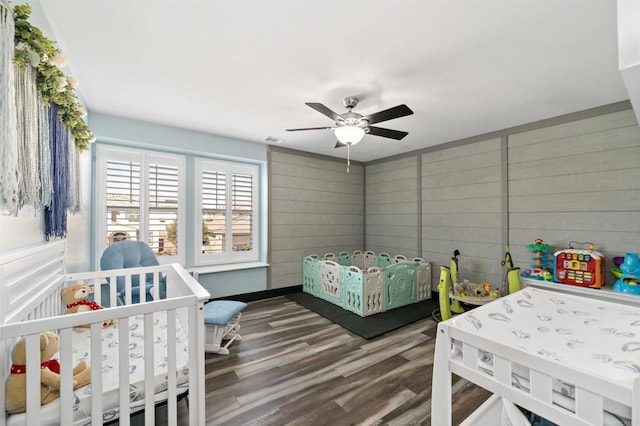 bedroom featuring ceiling fan, dark wood-type flooring, and wood walls