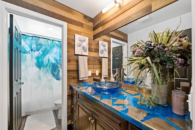 bathroom featuring a shower with shower curtain, vanity, toilet, and wooden walls