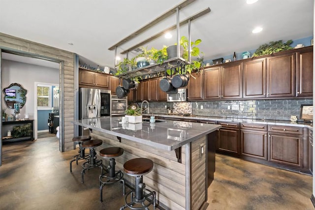 kitchen with a kitchen island with sink, stainless steel appliances, dark stone countertops, a breakfast bar area, and decorative backsplash