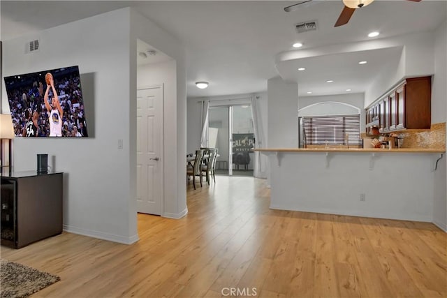 kitchen featuring a breakfast bar, tasteful backsplash, ceiling fan, kitchen peninsula, and light wood-type flooring