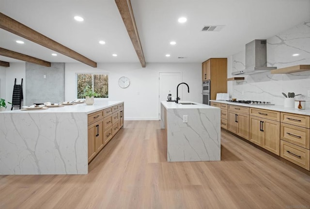 kitchen featuring a large island with sink, sink, wall chimney exhaust hood, and light wood-type flooring