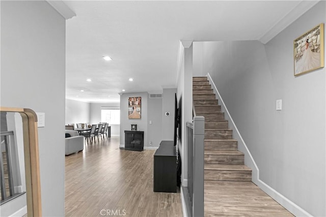 staircase with a fireplace, wood-type flooring, and ornamental molding