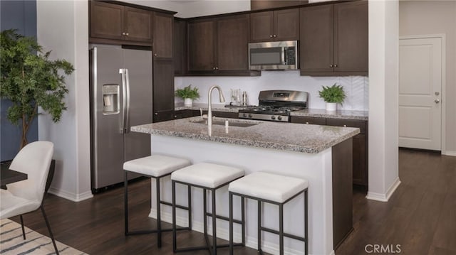 kitchen with light stone countertops, appliances with stainless steel finishes, dark hardwood / wood-style flooring, sink, and a center island with sink