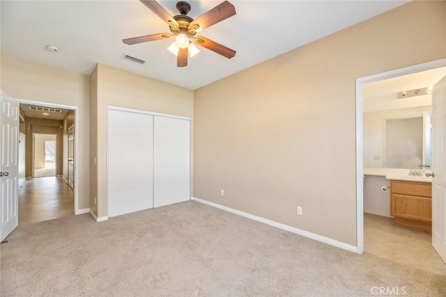 unfurnished bedroom featuring light carpet, a closet, connected bathroom, and ceiling fan