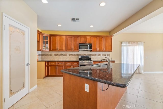 kitchen with light tile patterned flooring, stainless steel appliances, a kitchen island with sink, and sink