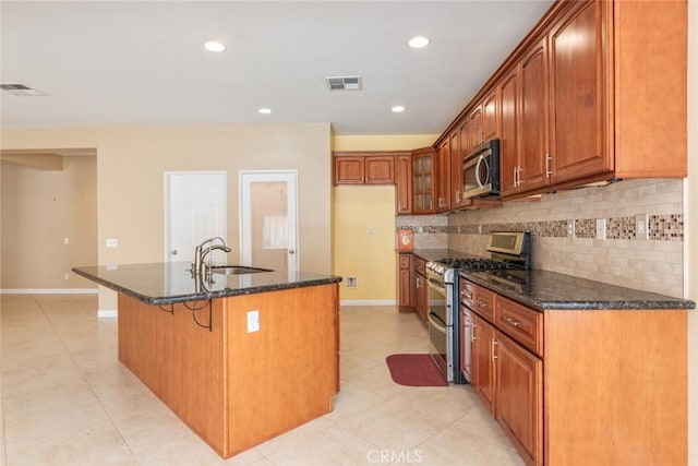 kitchen with a kitchen island with sink, appliances with stainless steel finishes, sink, and dark stone countertops