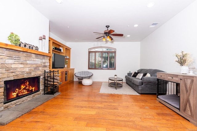 living room featuring ceiling fan, light wood-type flooring, and a stone fireplace