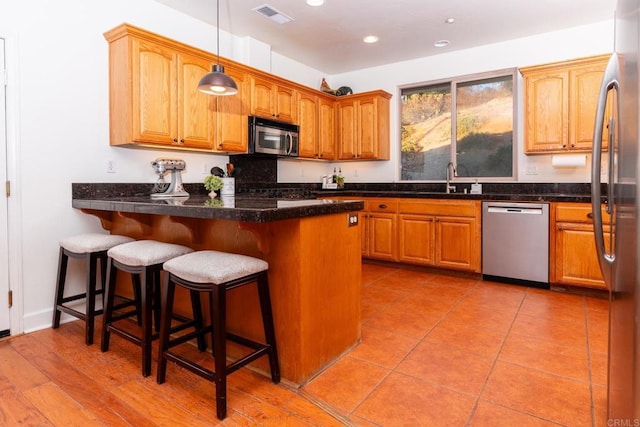 kitchen with kitchen peninsula, pendant lighting, appliances with stainless steel finishes, sink, and a kitchen bar