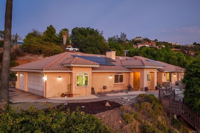 back house at dusk featuring a garage and solar panels