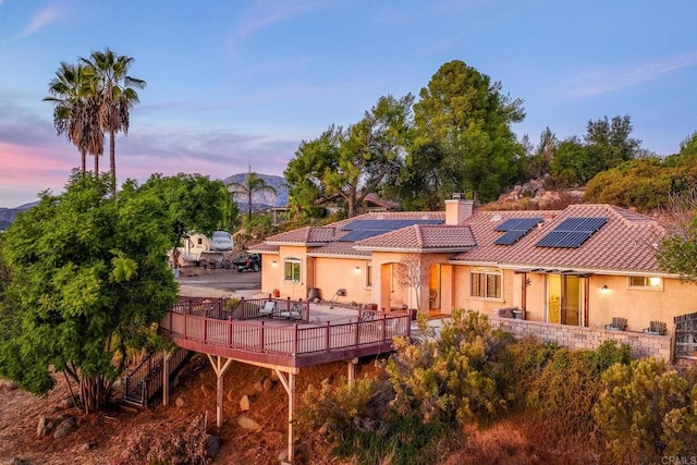 back house at dusk with a wooden deck and solar panels