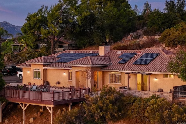 back house at dusk featuring a wooden deck and solar panels