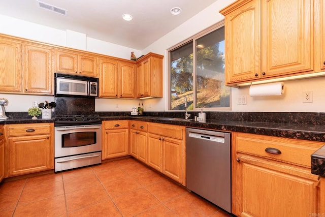 kitchen featuring sink, dark stone counters, light tile patterned floors, and stainless steel appliances