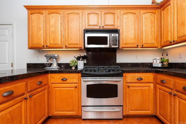 kitchen with light tile patterned floors, appliances with stainless steel finishes, and dark stone countertops