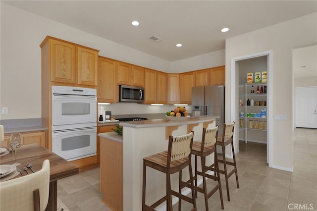 kitchen with a center island, stainless steel appliances, a kitchen bar, light brown cabinetry, and light tile patterned floors