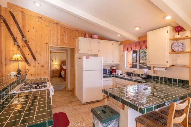 kitchen with tile countertops, white appliances, kitchen peninsula, vaulted ceiling with beams, and white cabinetry