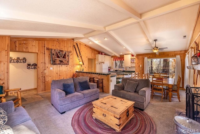 living room featuring vaulted ceiling with beams, ceiling fan, carpet floors, and wood walls