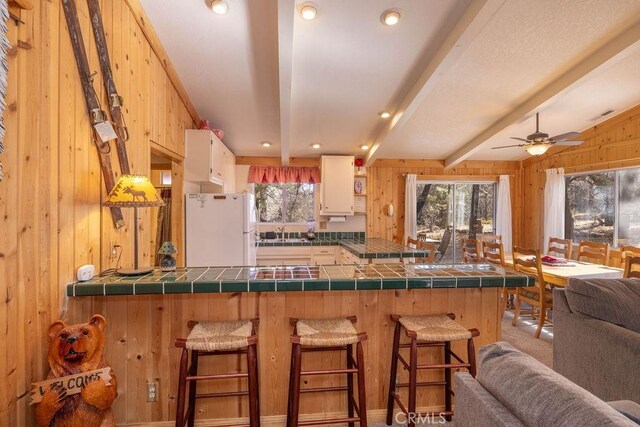 kitchen with a breakfast bar area, kitchen peninsula, wood walls, and white refrigerator