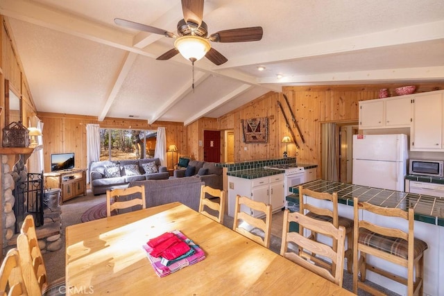 dining area with lofted ceiling with beams, wood walls, wood-type flooring, and ceiling fan