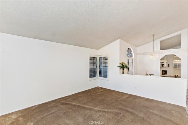 carpeted spare room with a large fireplace, lofted ceiling, a notable chandelier, and a textured ceiling