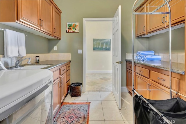 kitchen with washer / dryer, light tile patterned floors, light stone counters, and sink