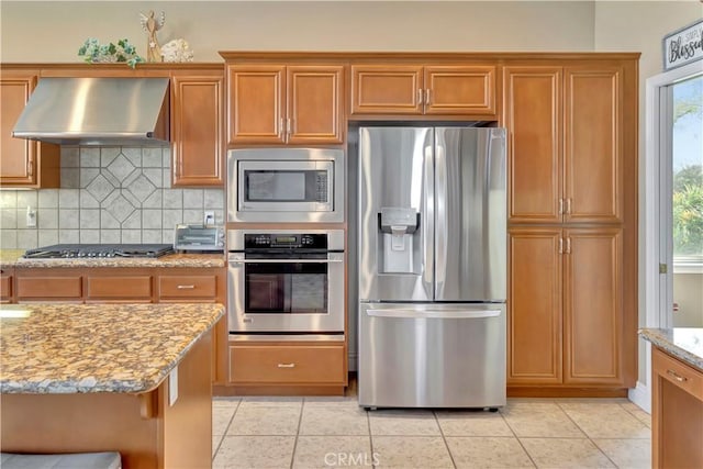 kitchen with light stone counters, light tile patterned flooring, wall chimney range hood, and appliances with stainless steel finishes