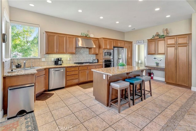 kitchen with a kitchen bar, light stone counters, stainless steel appliances, wall chimney range hood, and a kitchen island