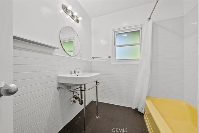 bathroom featuring wood-type flooring, sink, shower / bathtub combination with curtain, and tile walls