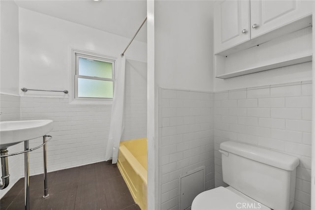 bathroom with hardwood / wood-style flooring, toilet, shower / bathtub combination with curtain, and tile walls