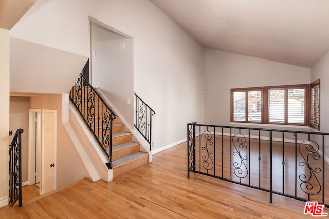 stairs with high vaulted ceiling and wood-type flooring