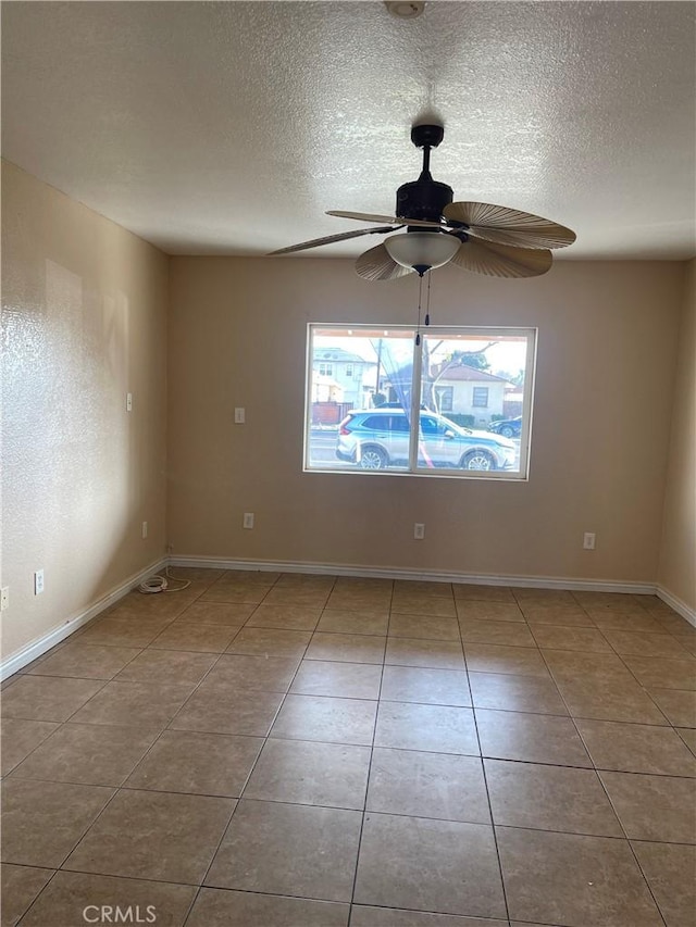 tiled empty room featuring baseboards, a textured ceiling, and ceiling fan