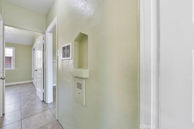 hall featuring light tile patterned flooring, visible vents, and a textured wall