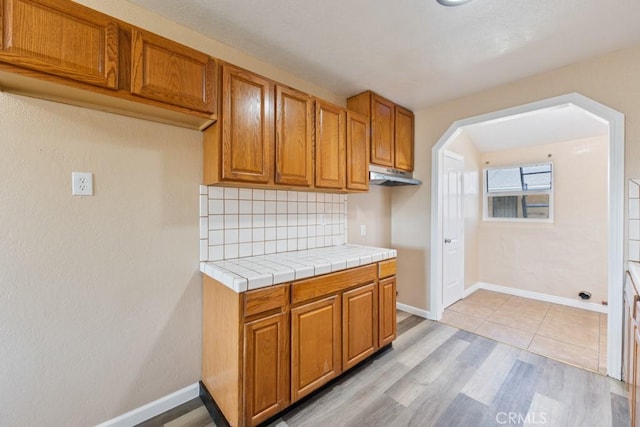 kitchen with backsplash, baseboards, light wood-style floors, and brown cabinets