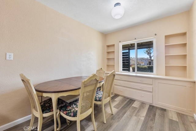 dining room with baseboards, light wood-style floors, and a textured wall