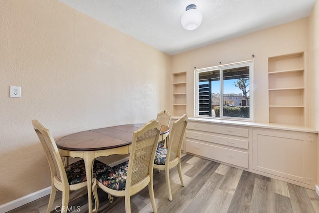 dining room featuring baseboards, light wood-style floors, and a textured wall