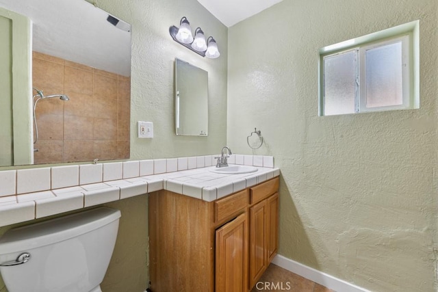 full bath featuring baseboards, toilet, tiled shower, a textured wall, and vanity